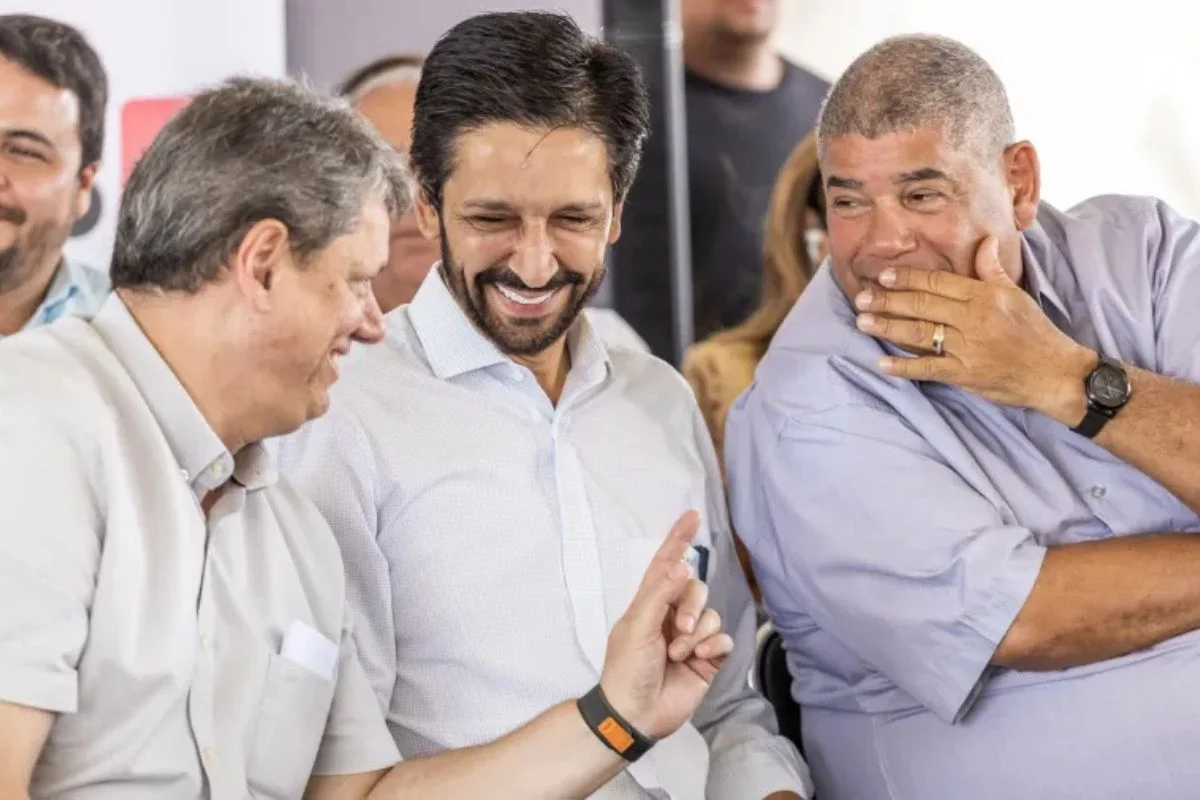 imagem colorida mostra três homens conversando. na ponta esquerda está tarcísio de freitas. ele veste uma camisa de manga curta e cor clara, e está sorrindo. no meio está ricardo nunes. ele veste uma camisa branca de manga longa e dá risada. à direita está milton lete. ele usa uma camisa de manga curta na cor azul e tem a mão cobrindo a boca