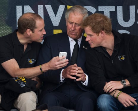 Prince William holding a smartphone up to show the king and Prince Harry, with the Invictus Games logo in the background