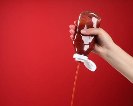 A hand squeezes ketchup out of a bottle against a red background